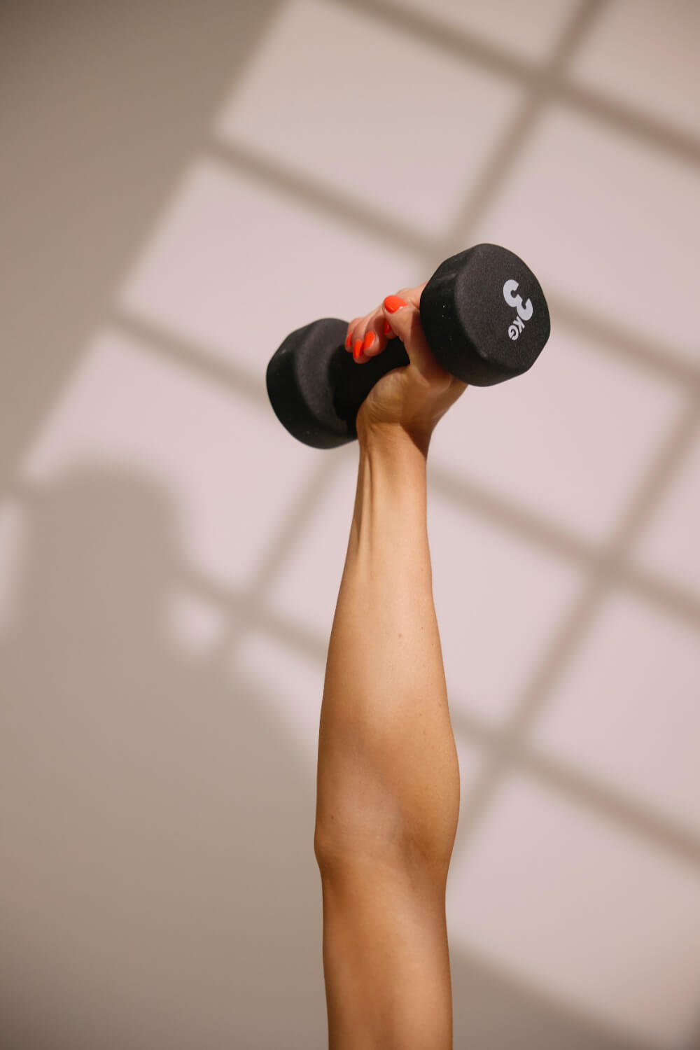  Close up of an extended arm holding a black 3kg weight